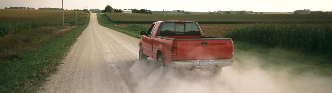 A red pickup truck driving down a dusty country road