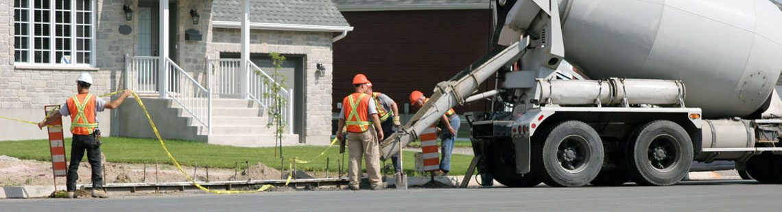 Road construction crew pouring concrete from a concrete mixer truck in a residential neighborhood